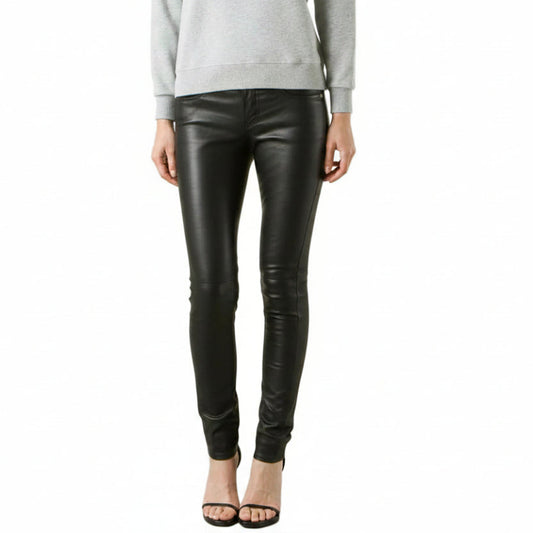 A model from the waist down wearing black lambs leather skinny pants with a tonal graphic print on the lower left leg, paired with a light gray sweatshirt and black high-heeled sandals, against a plain white background.