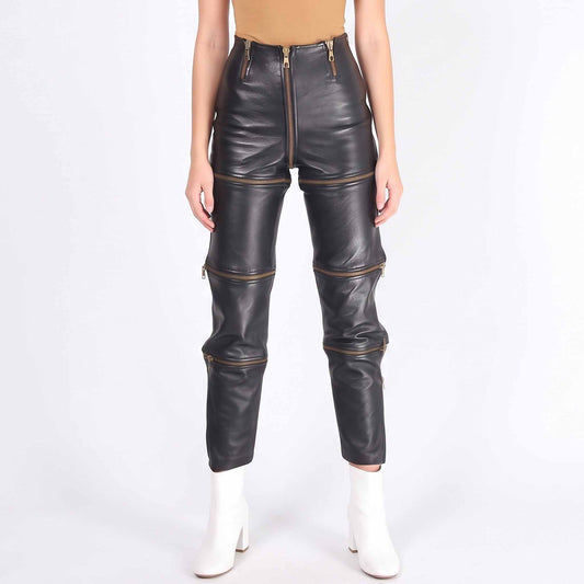 Direct front view of female model in black leather zip off trousers showing center zipper and gold horizontal leg zippers
