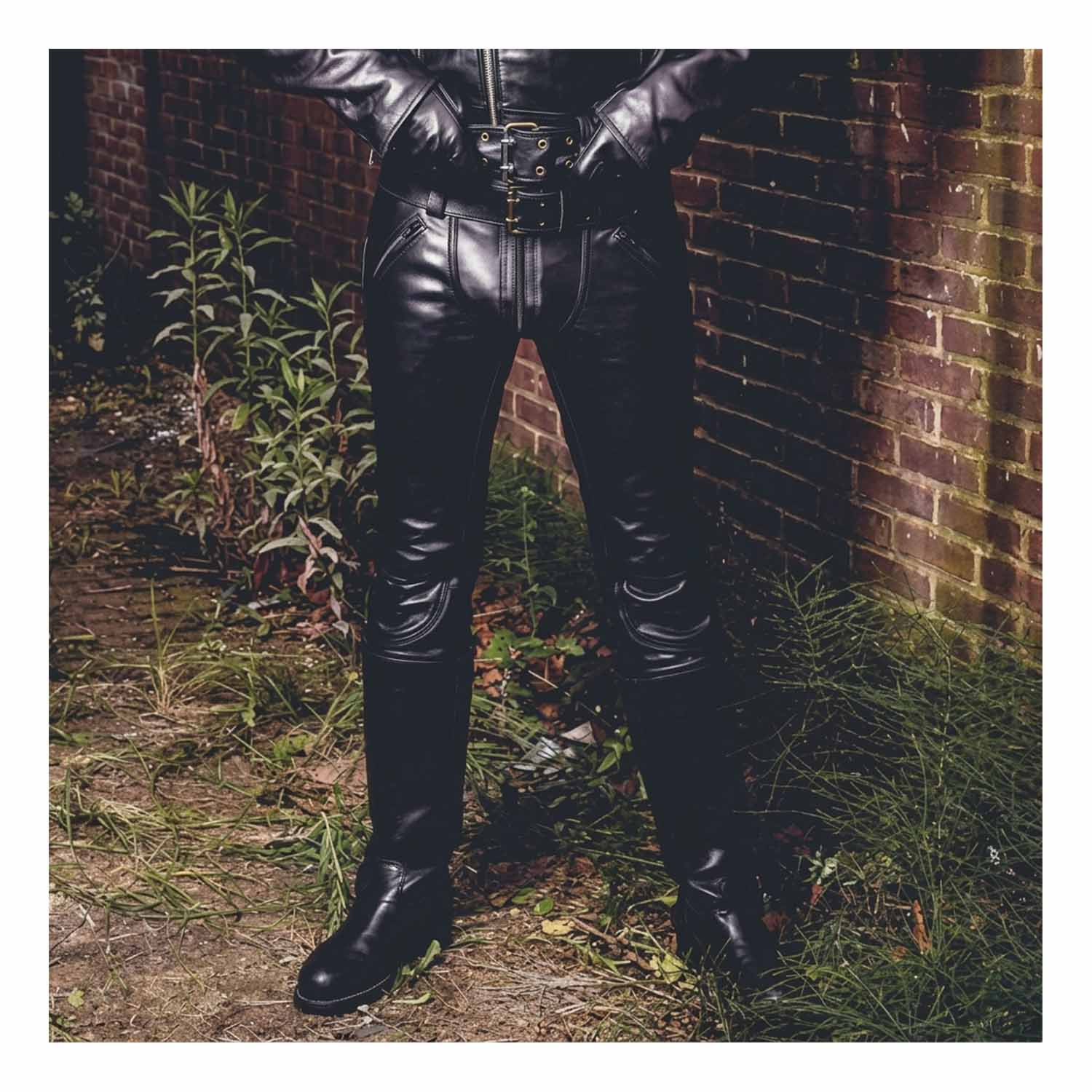 Front outdoor view of a man wearing black cowhide leather slim-fit breeches with double zippers tucked into tall biker boots.