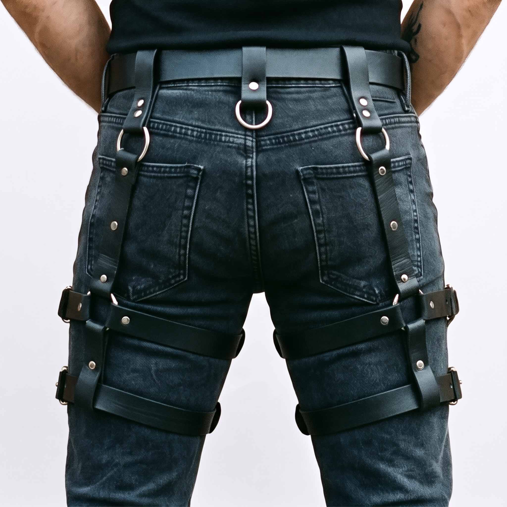 Rear perspective of male model displaying black leather thigh harness showing back belt loops, center O ring, and horizontal leg straps