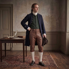 Full length view of colonial gentleman wearing brown leather 18th century breeches navy frock coat and white stockings standing in period room