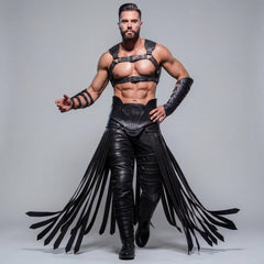 Front view of athletic warrior model posing in black cowhide leather chest harness, armored forearm bracers, and dramatic leather fringe girdle