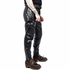 Side profile view of men's slim-fit leather motorcycle trousers featuring brass ankle zips and quilted knee padding paired with brown leather boots.