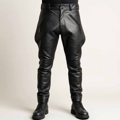 Front view of a man wearing black cowhide leather breeches featuring a flared thigh design, zippered front pockets, and structured waistband paired with boots.