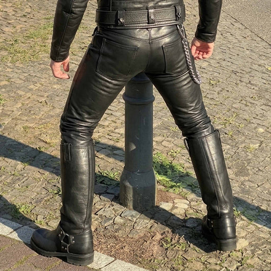 Rear view of a person wearing black leather pants and tall black leather boots on a cobblestone street, with a black leather jacket also visible.