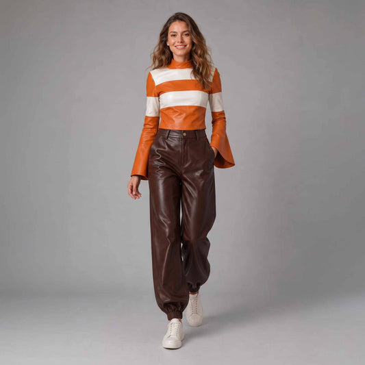 Front walking pose highlighting the draped fit and elastic ankle cuffs of the women's brown leather jogger trousers and matching striped cropped leather top