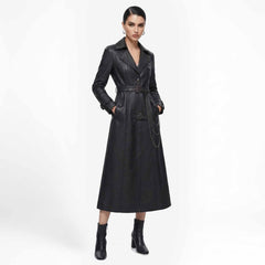 Front view of a woman wearing a long black leather trench coat with a belted waist and hanging chain detail, paired with heeled boots.
