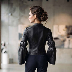 Back full view of woman wearing tailored black leather blouse showing contoured back seams and gathered bell sleeve construction