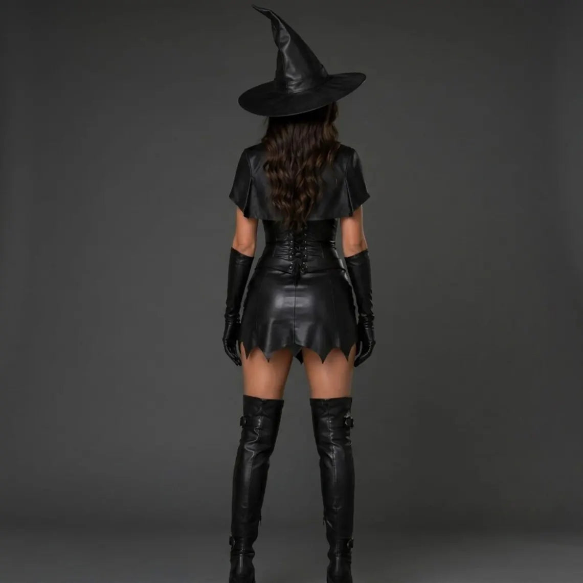 Rear view of women's black leather witch costume highlighting the adjustable lace-up back corset, short capelet, and scalloped dress hem.